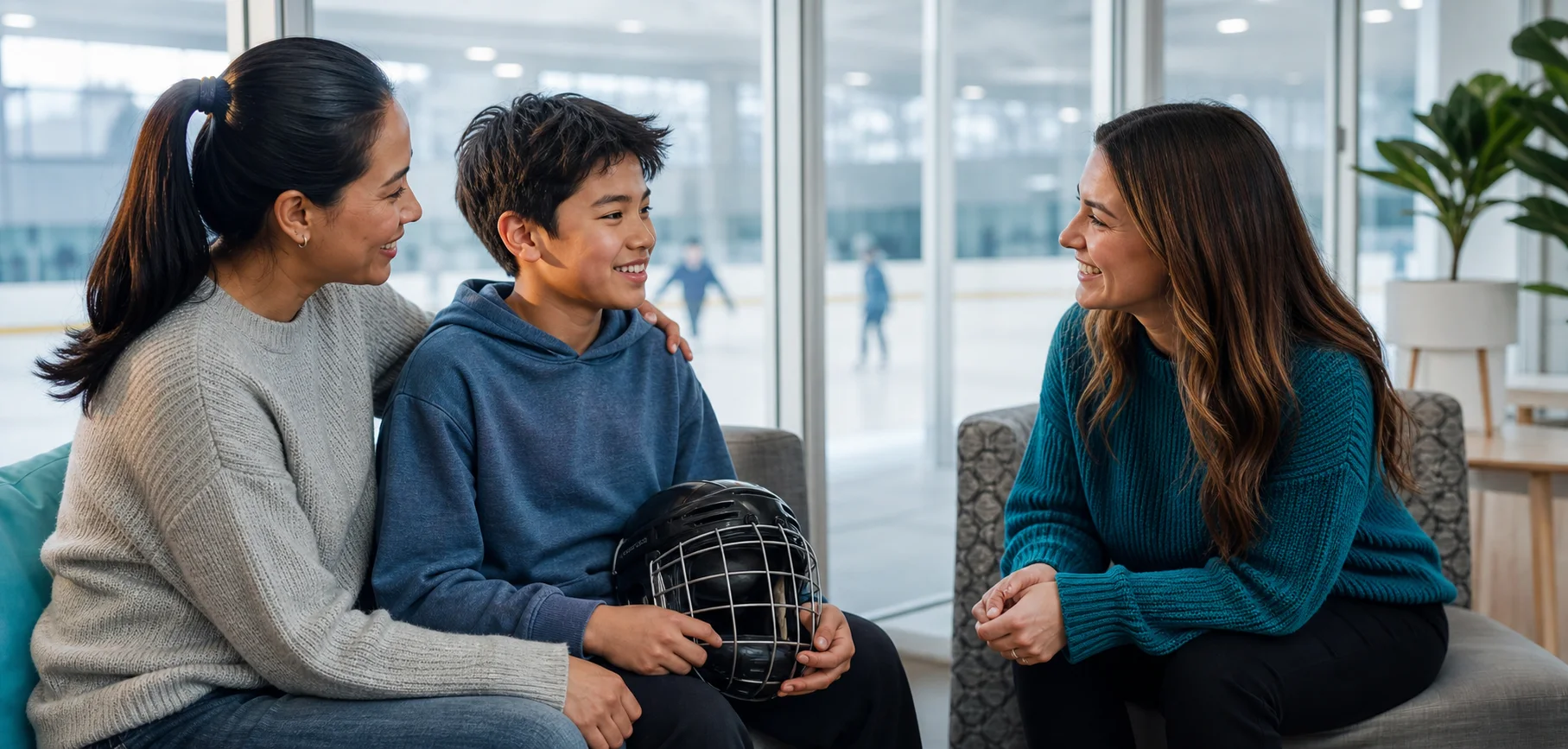 A child holding a hockey helmet with a parent and care professional beside an ice rink